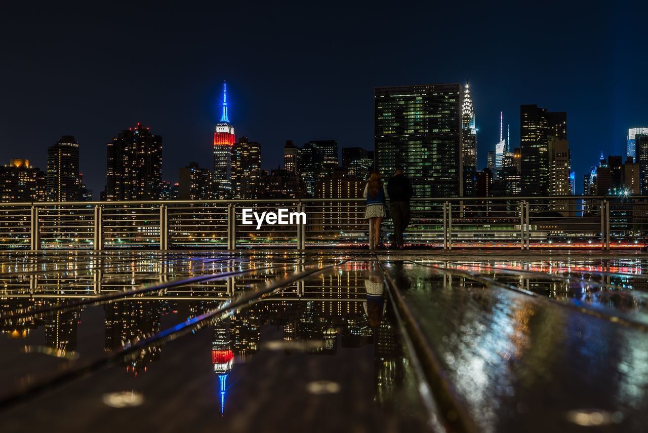 Rear view of man and woman at gantry plaza state park in city during night