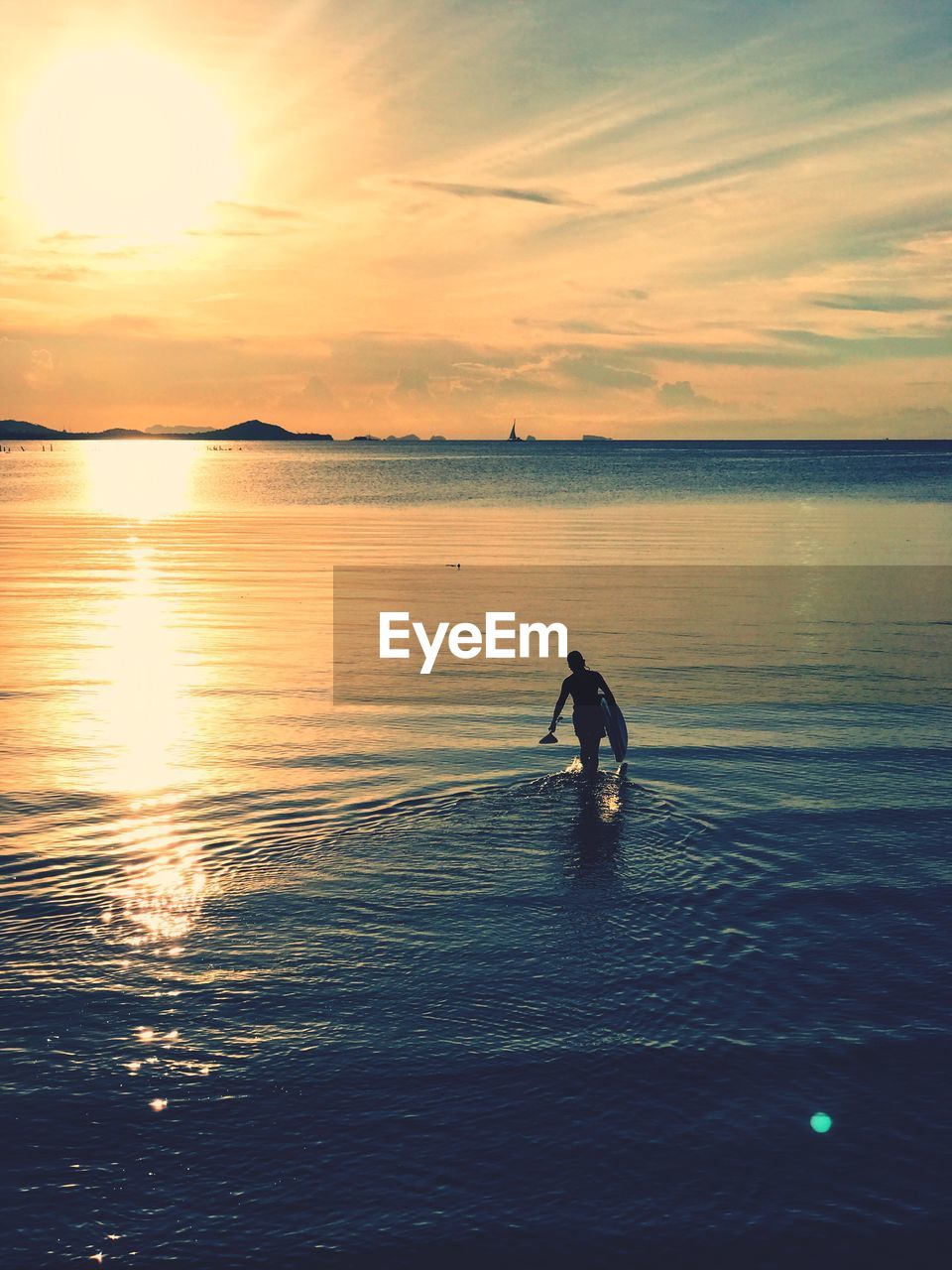 Silhouette woman with surfboard wading in sea against sky during sunset