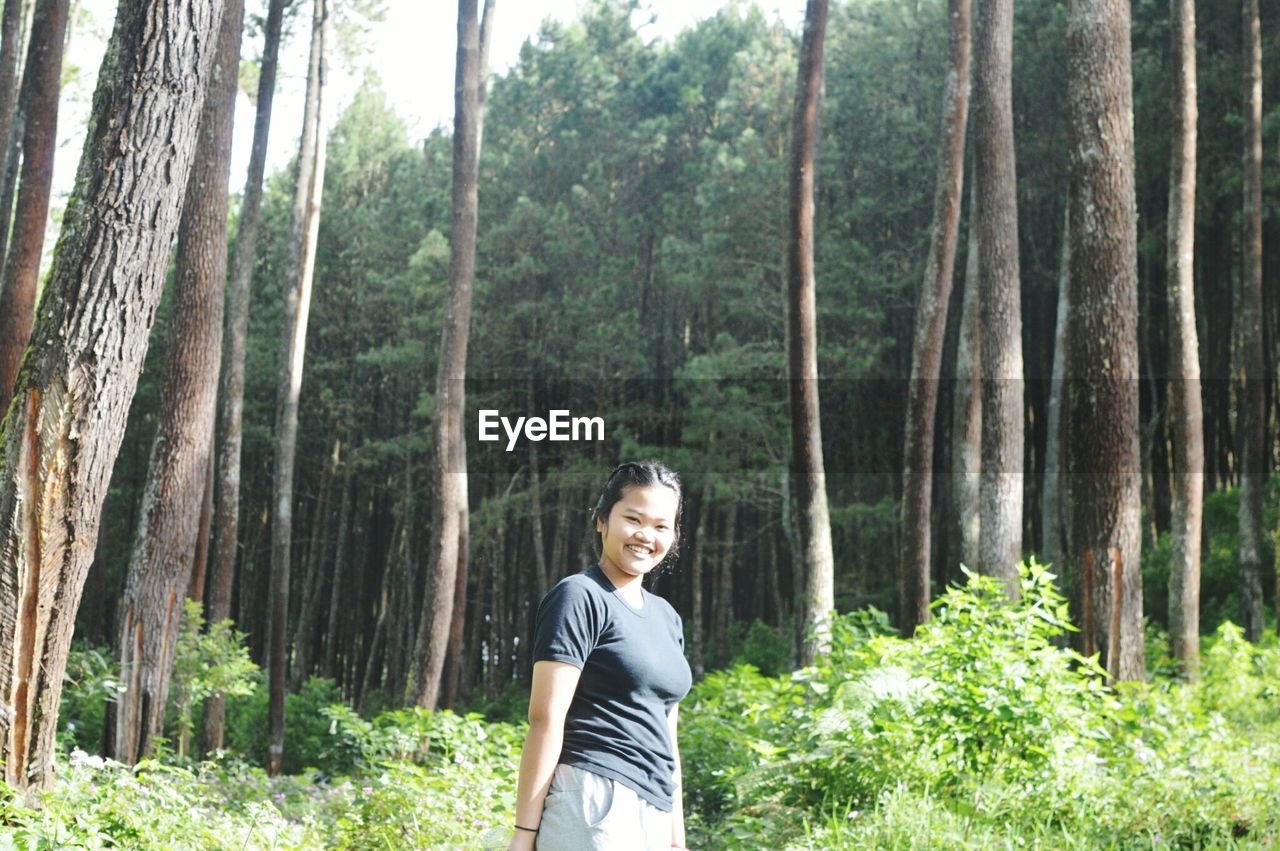 Portrait of smiling woman standing against trees at forest