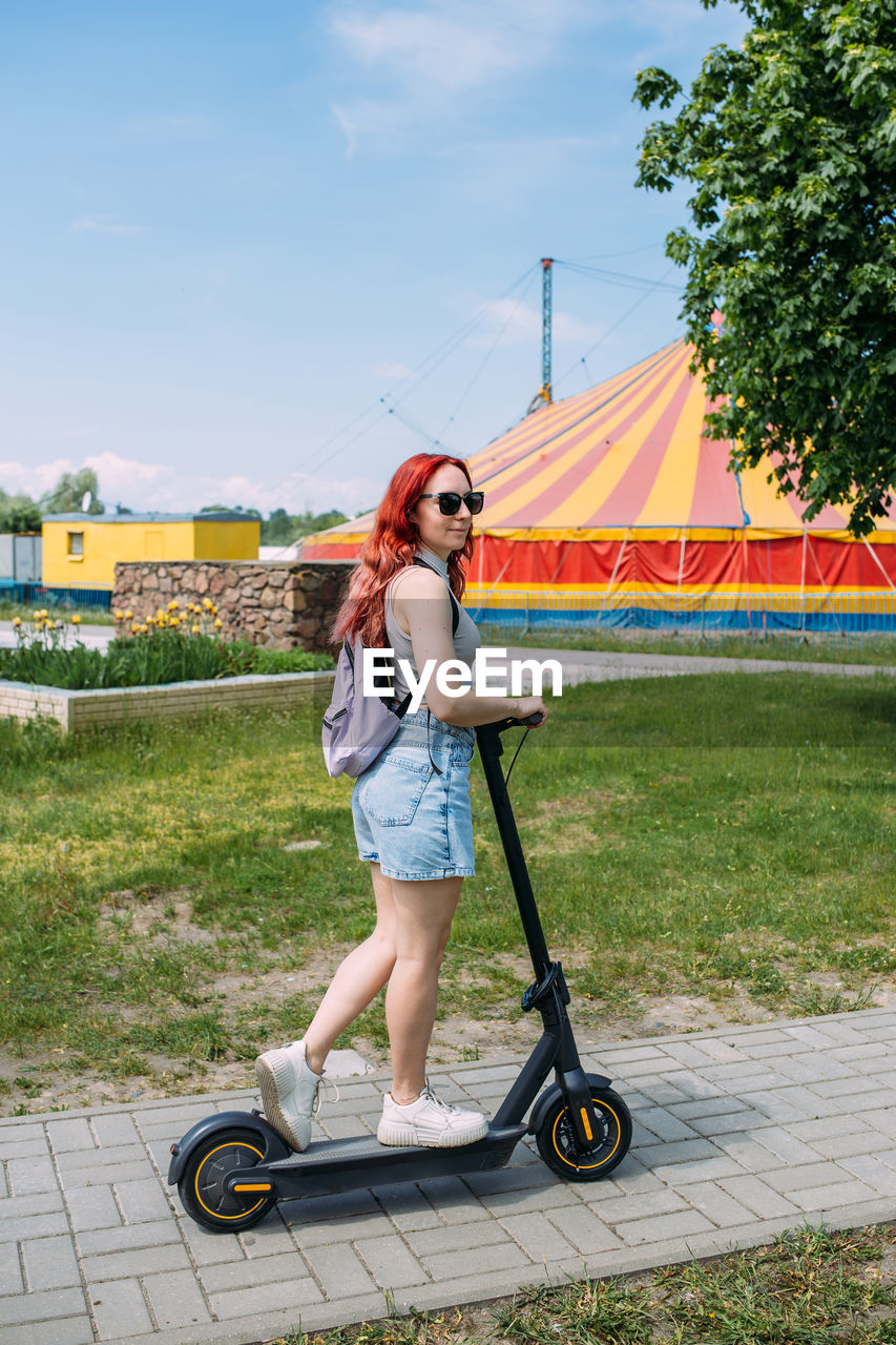 Young bright woman smiles and rides electric scooter in the summer in the city