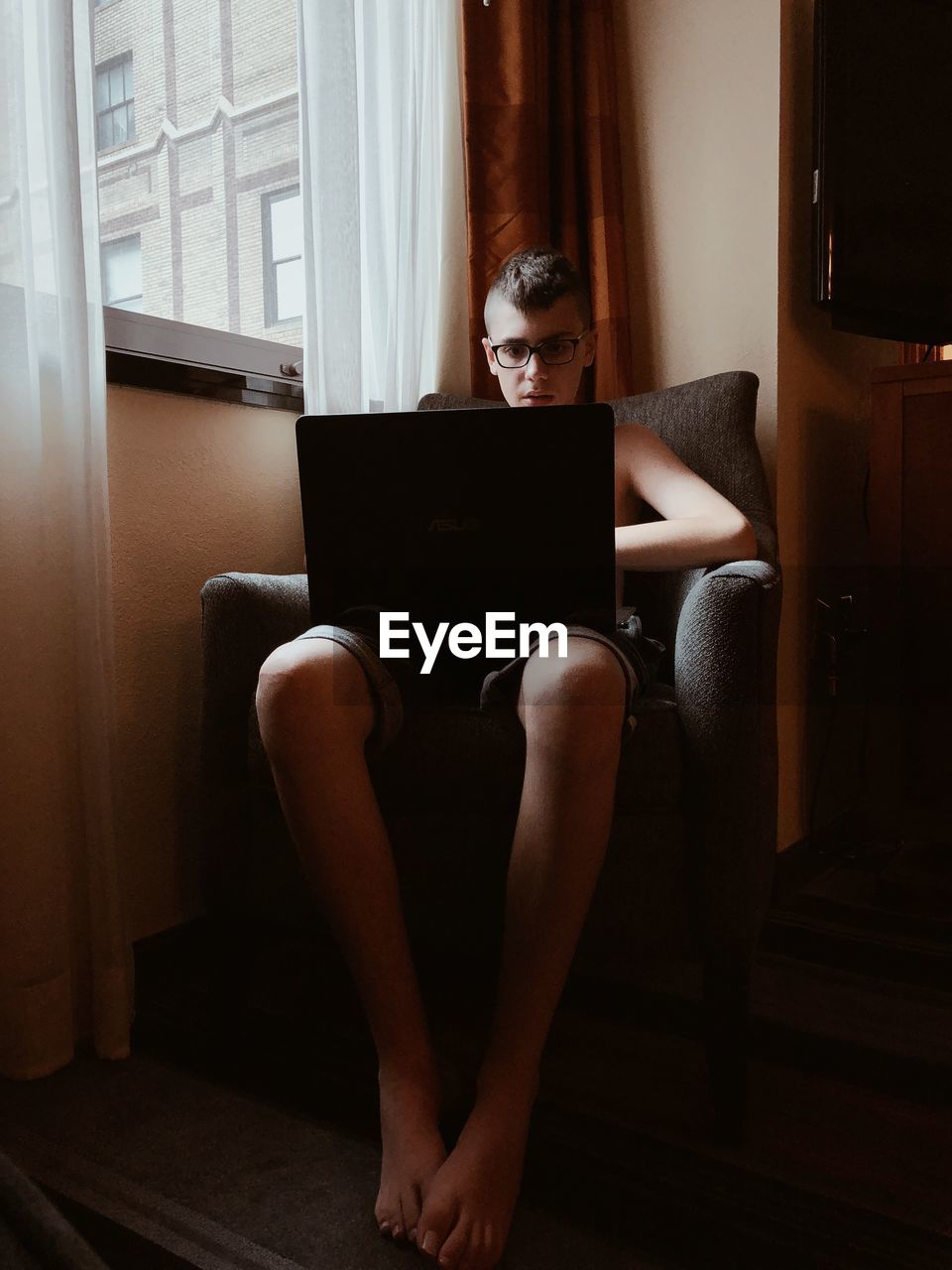 Teenage boy using laptop while sitting on armchair at home