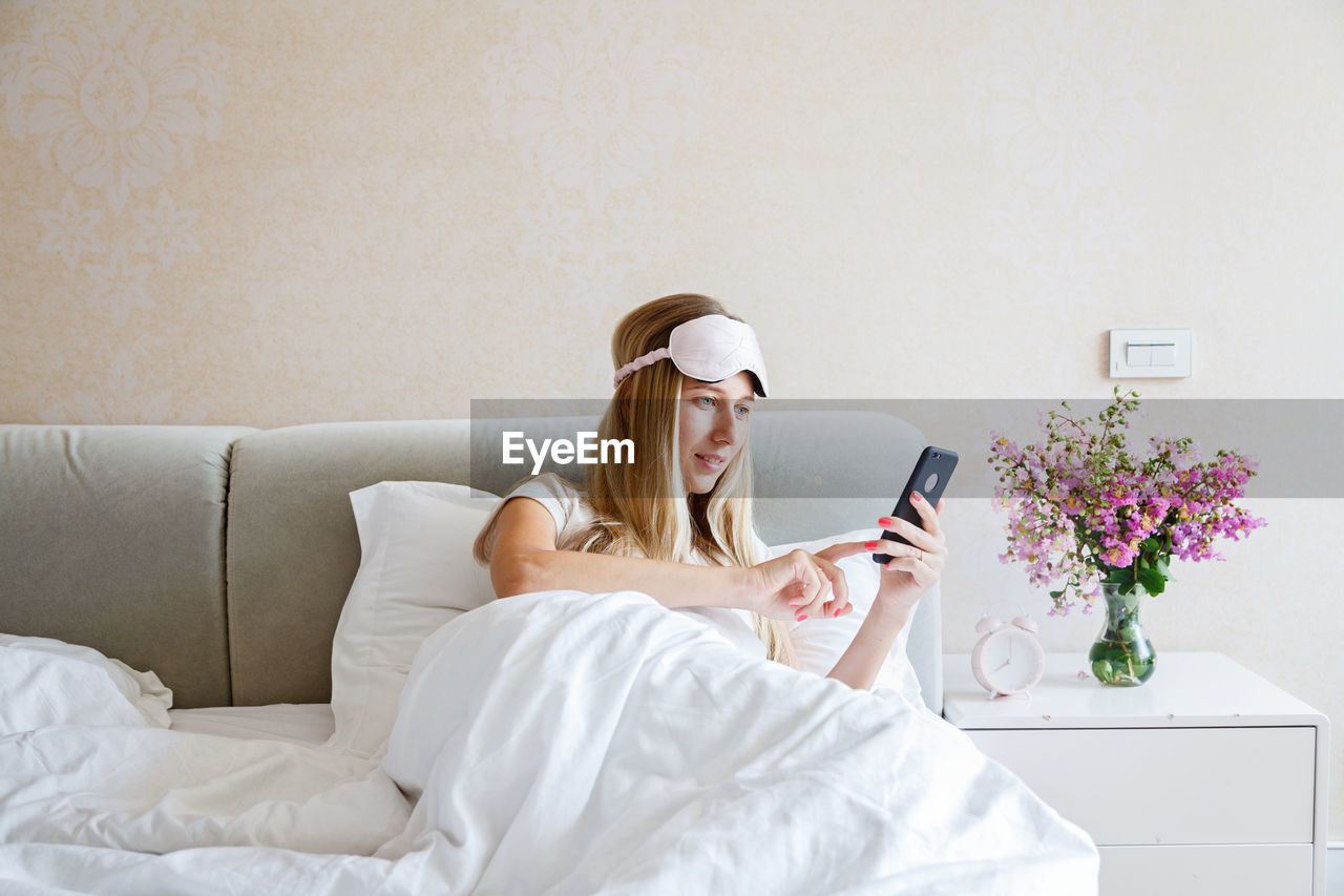 Young woman using smart phone while relaxing on bed at home