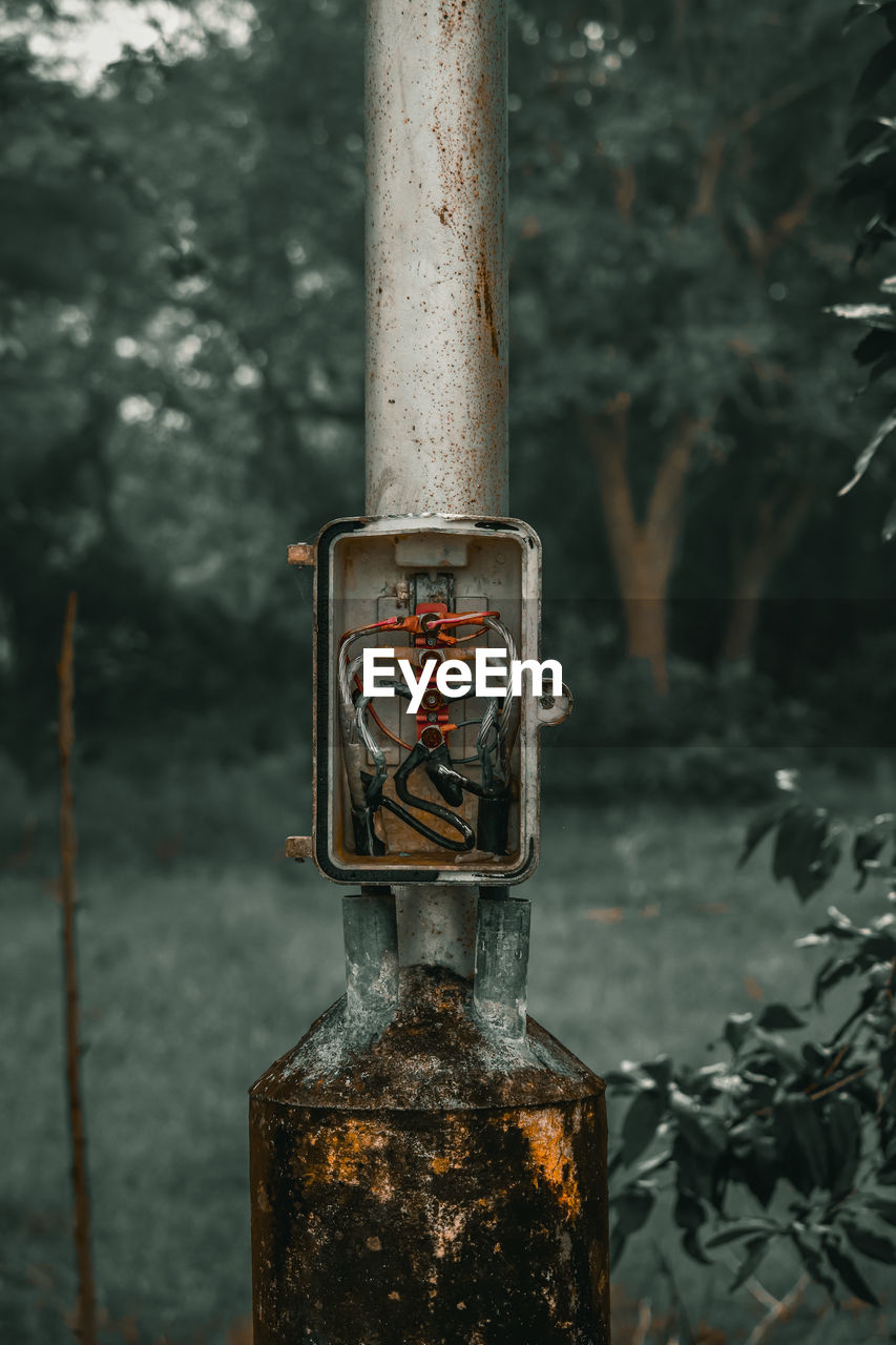 Close-up of old metal pole against trees