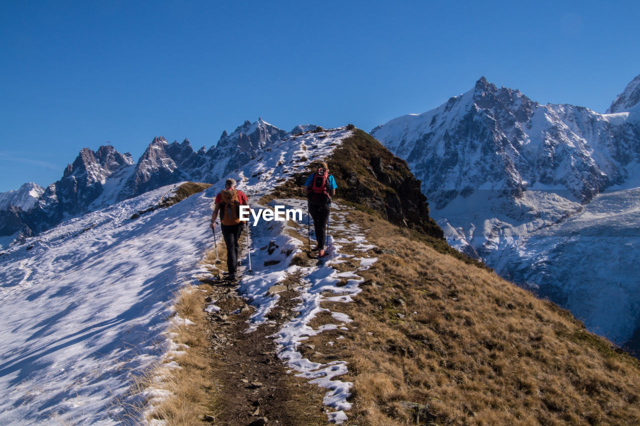 Rear view of hikers climbing snow covered mountains against clear blue sky