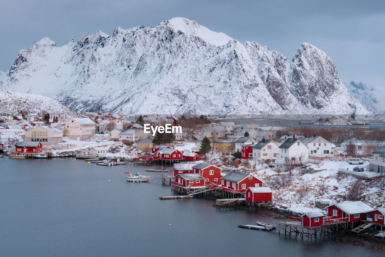 High angle view of houses by river against snowcapped mountain during winter