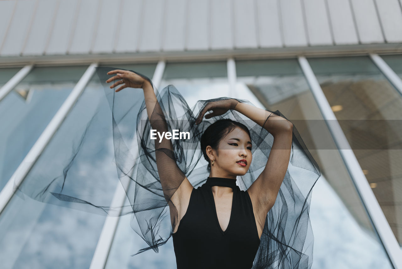 Low angle view of beautiful woman with arms raised standing against building