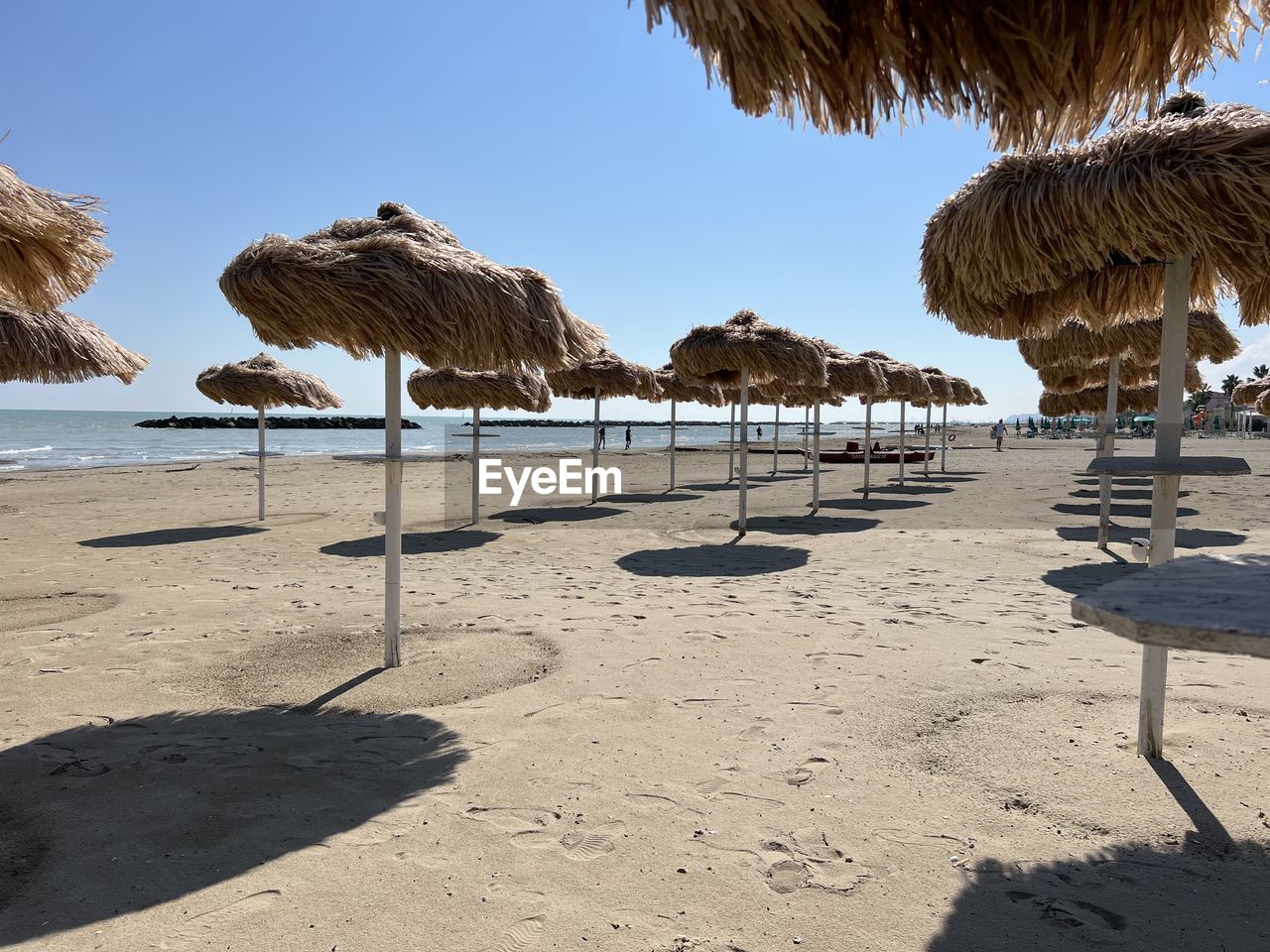 land, beach, sand, thatched roof, nature, water, sky, sea, sunlight, shore, shadow, ocean, coast, beauty in nature, tranquility, scenics - nature, sunny, tropical climate, shade, day, palm tree, tranquil scene, vacation, holiday, roof, travel destinations, trip, clear sky, body of water, chair, hut, summer, parasol, no people, tree, outdoors, blue, beach umbrella, travel, relaxation, idyllic, sunshade, plant, environment