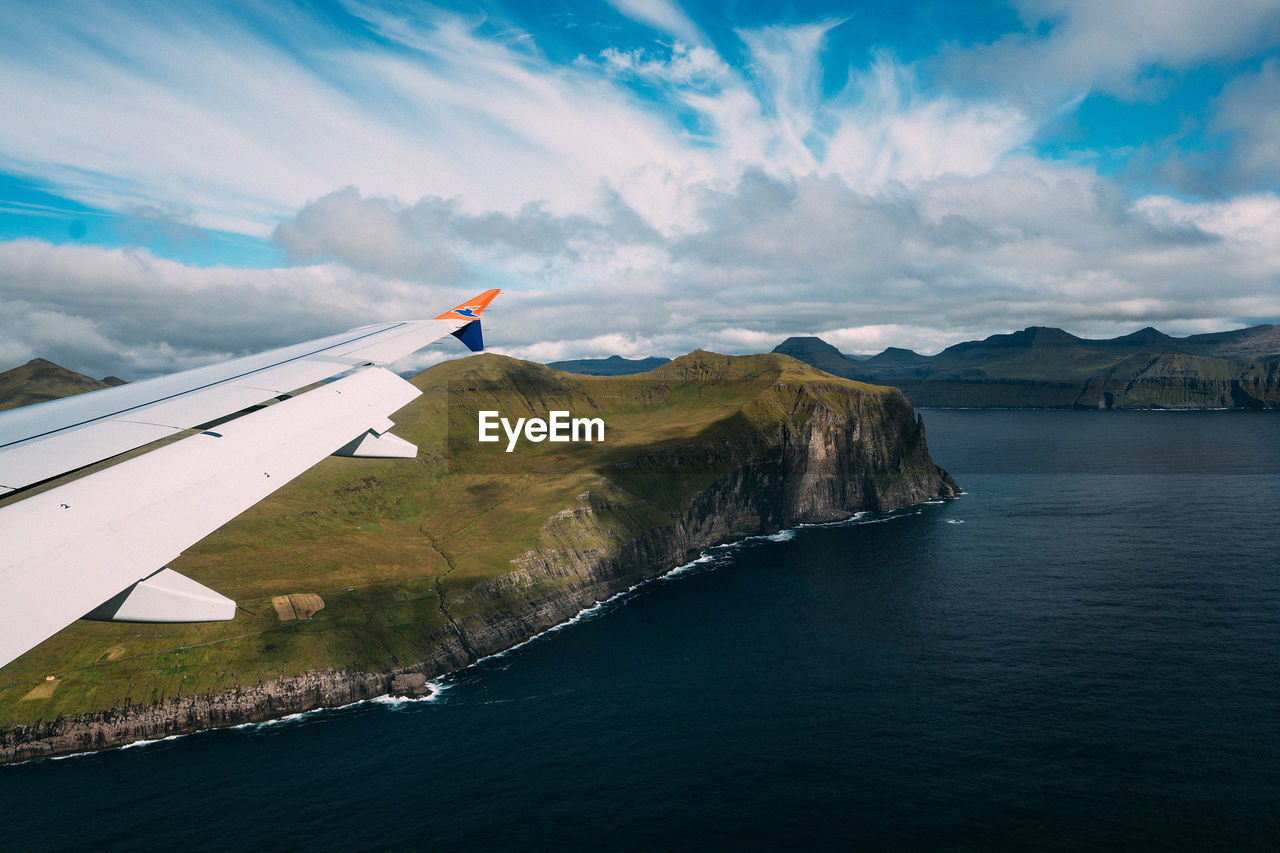 SCENIC VIEW OF SEA AND AIRPLANE FLYING OVER MOUNTAINS AGAINST SKY