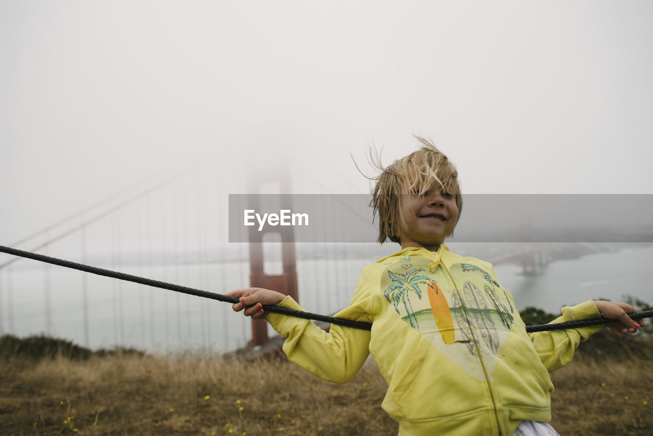 Girl leaning on cable against golden gate bridge during foggy weather