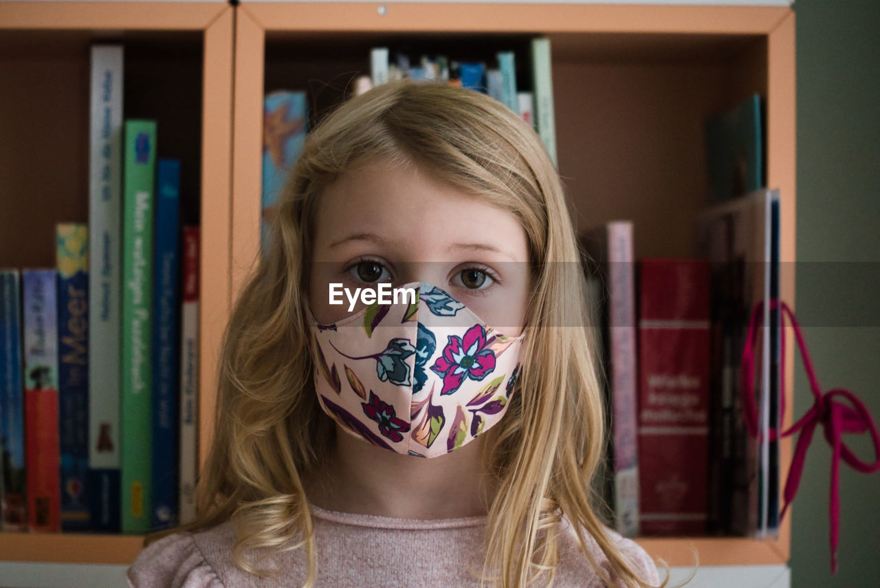 Close-up portrait of cute girl wearing mask standing at home