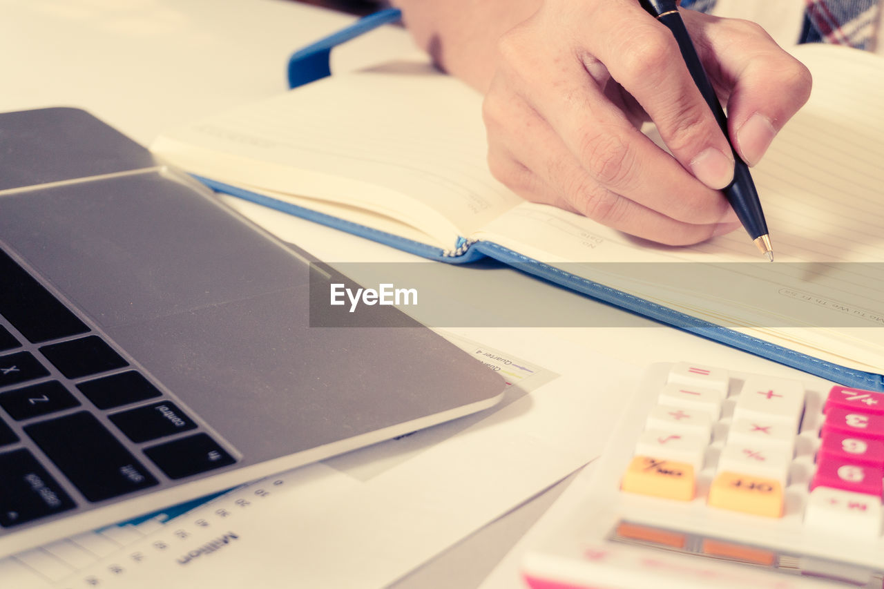 Cropped image of man writing on book at office