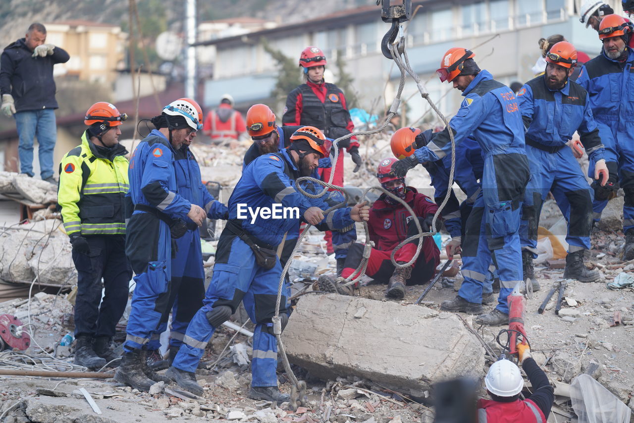 group of people, men, working, occupation, cooperation, teamwork, adult, protective workwear, clothing, headwear, day, protection, helmet, large group of people, standing, manual worker, industry, crowd, person, coworker, outdoors, security, hat, reflective clothing, young adult, full length, group, togetherness