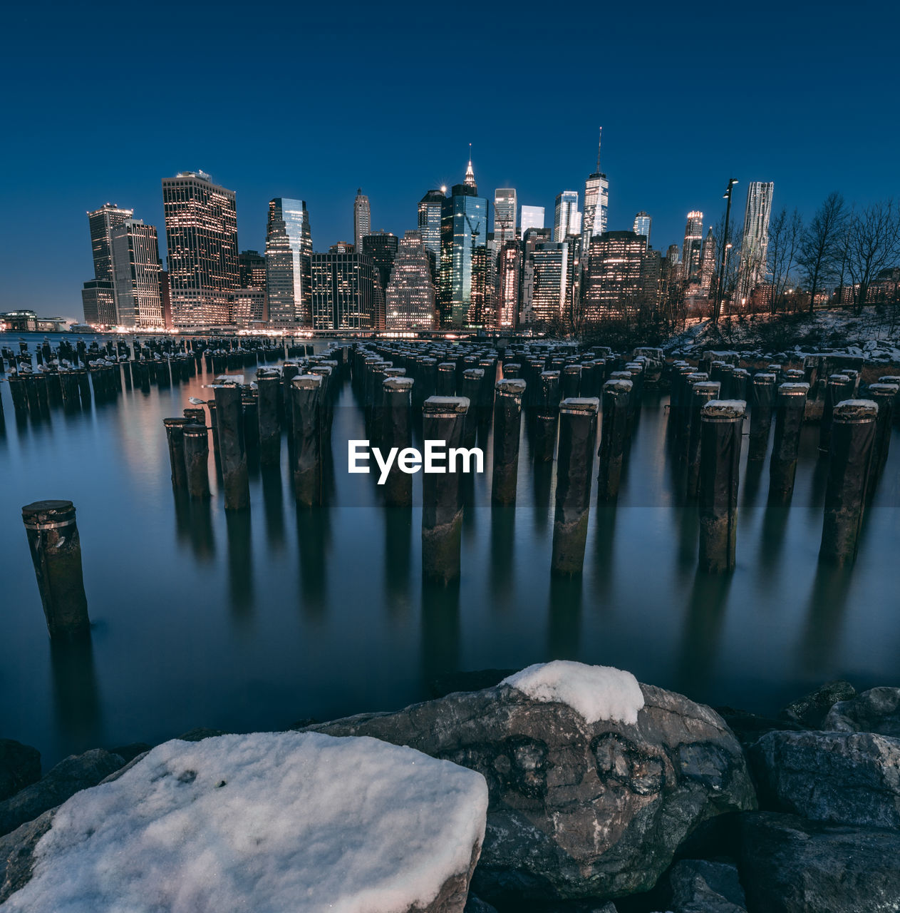 Wooden posts in river against illuminated building at night