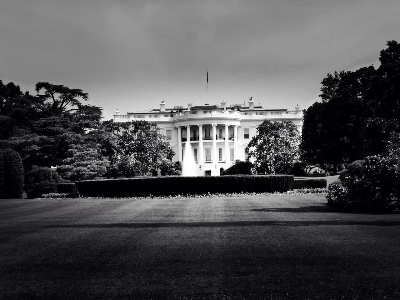 Fountain in front of white house against cloudy sky