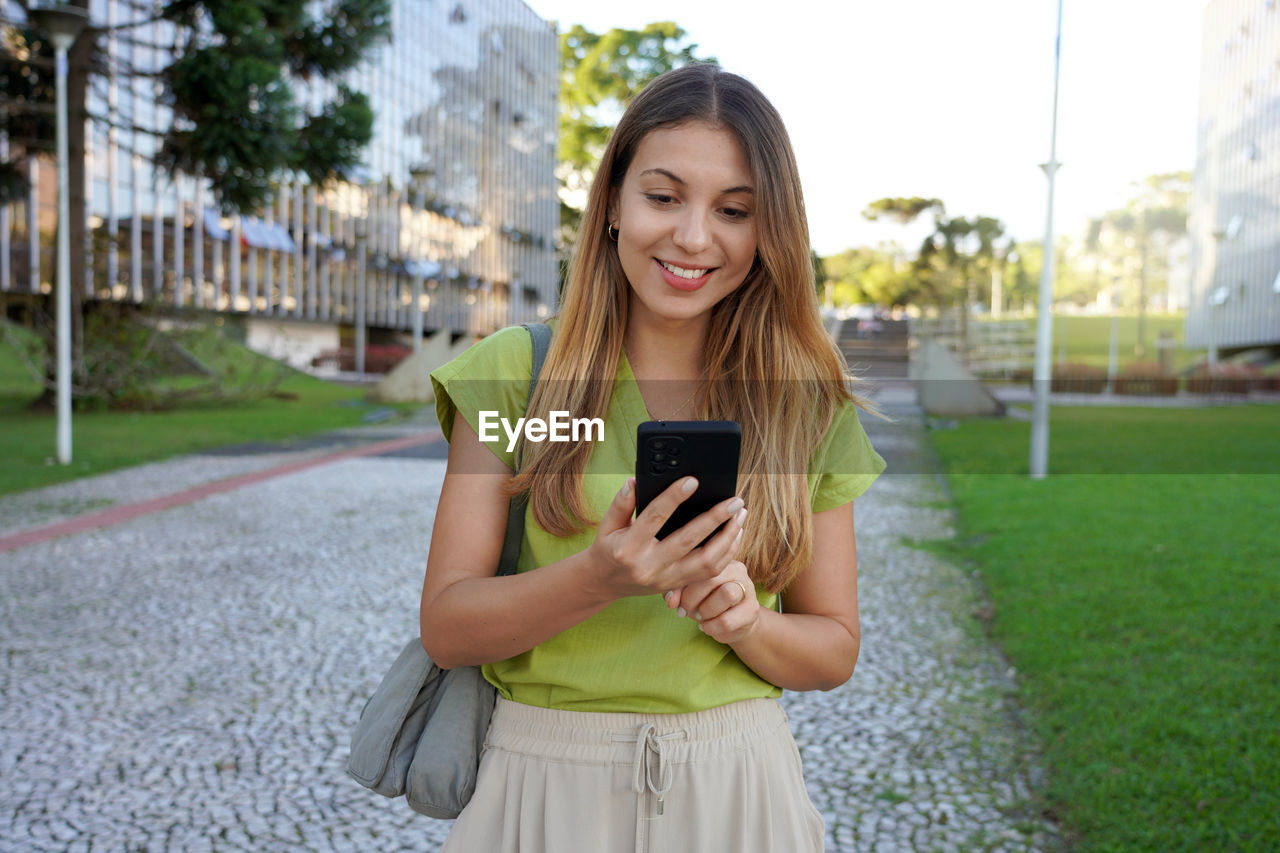 Brazilian woman walking using cell phone texting in city street of curitiba on sunset, parana brazil