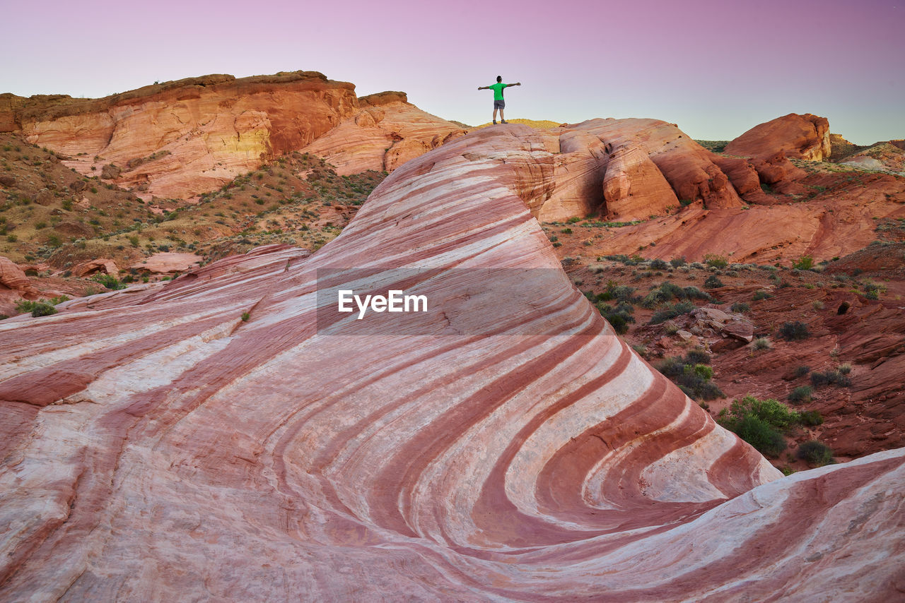 Distant view of man standing on rock formations during sunset