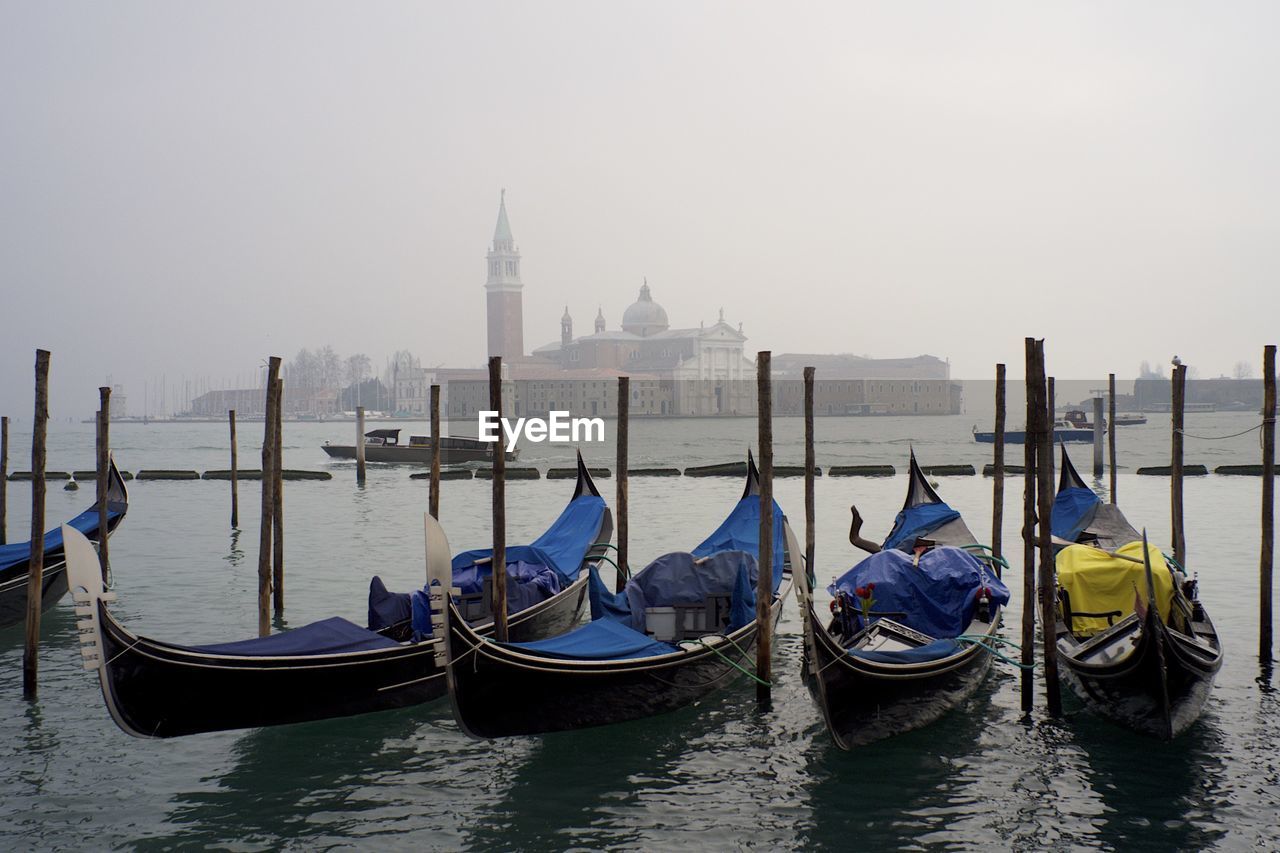 Gondolas moored in grand canal against san giorgio maggiore during foggy weather