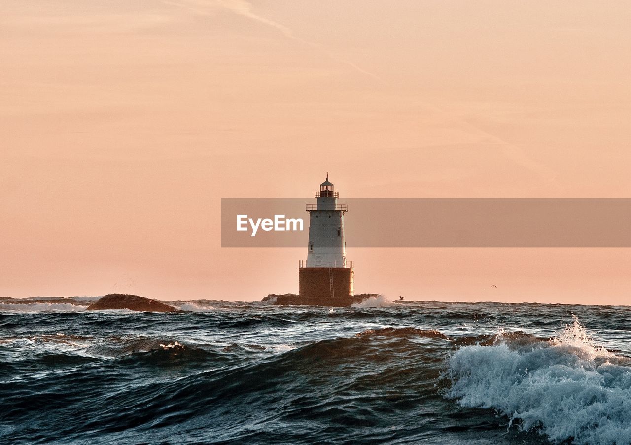 Lighthouse by sea against clear sky