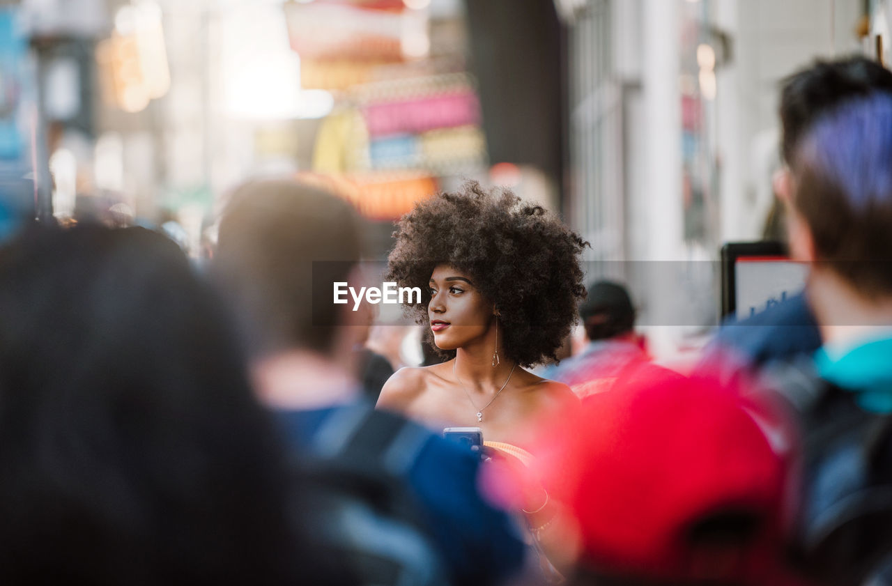 Young woman looking away while holding smart phone on city street