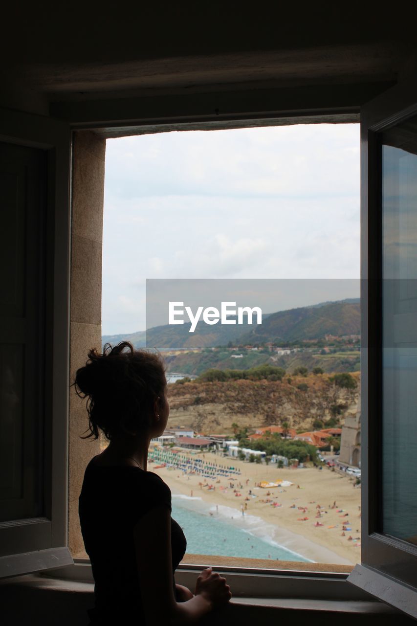 Rear view of woman looking through window over the sea