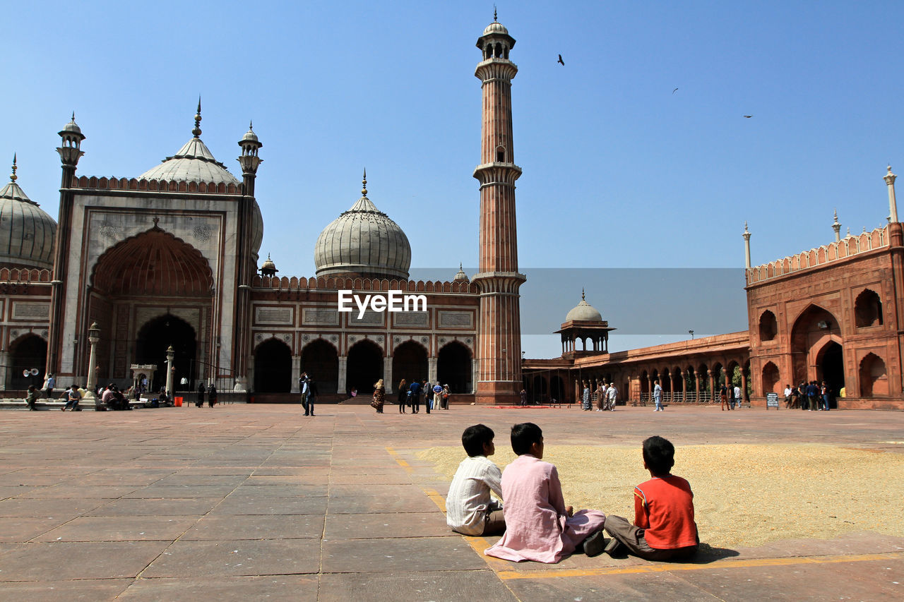 Rear view of boys sitting outside jama masjid in city