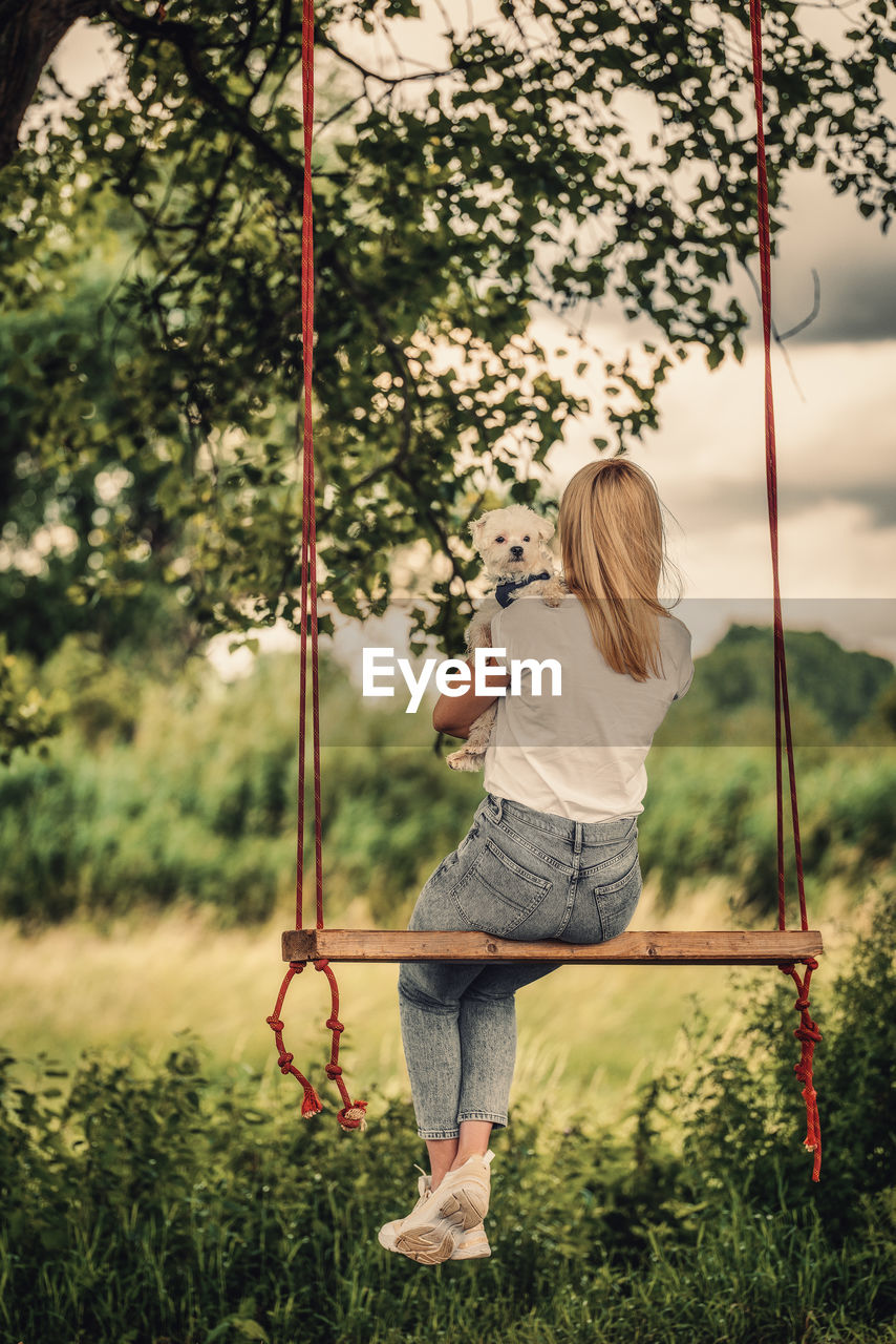 Young woman with a white dog on a tree swing.