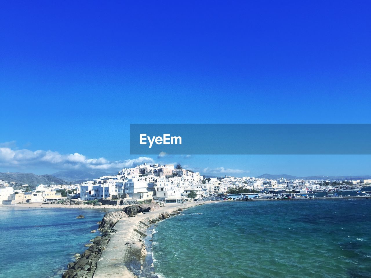 Pier amidst sea leading towards city against clear blue sky