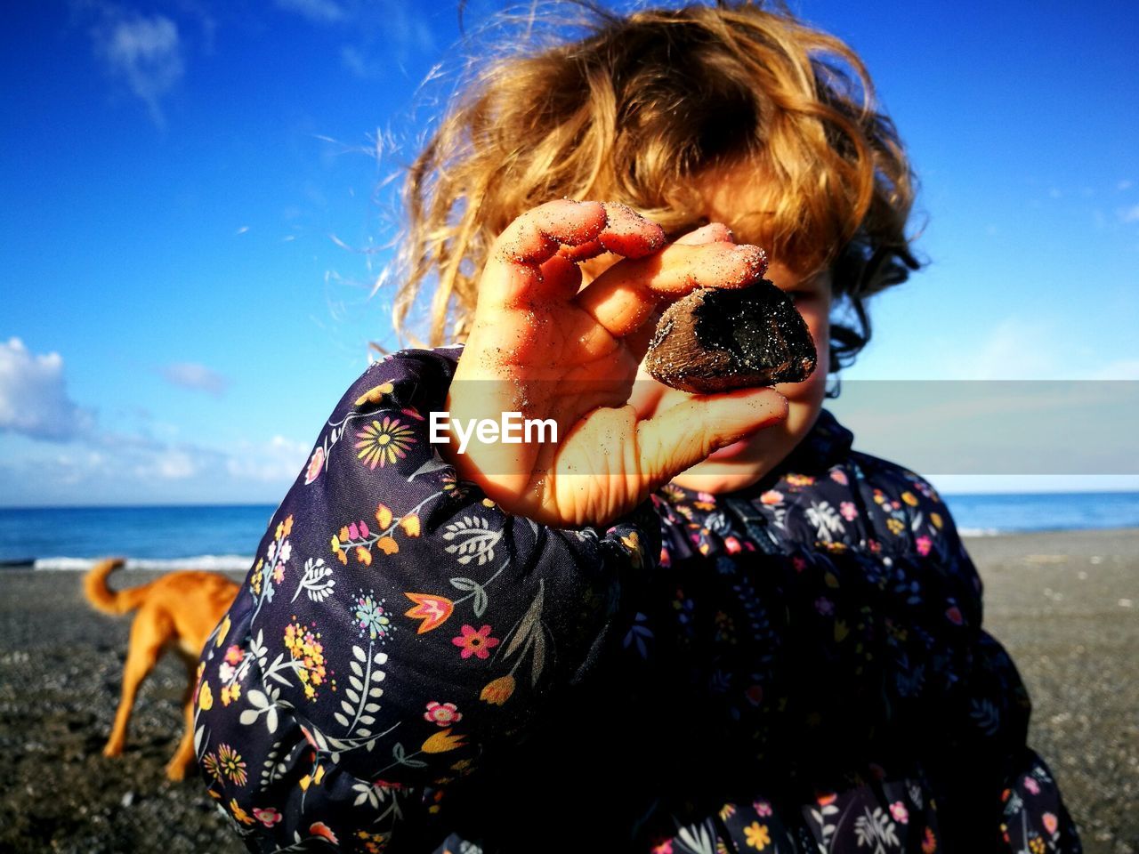 Close-up of cute girl holding stone over face while standing at beach against sky