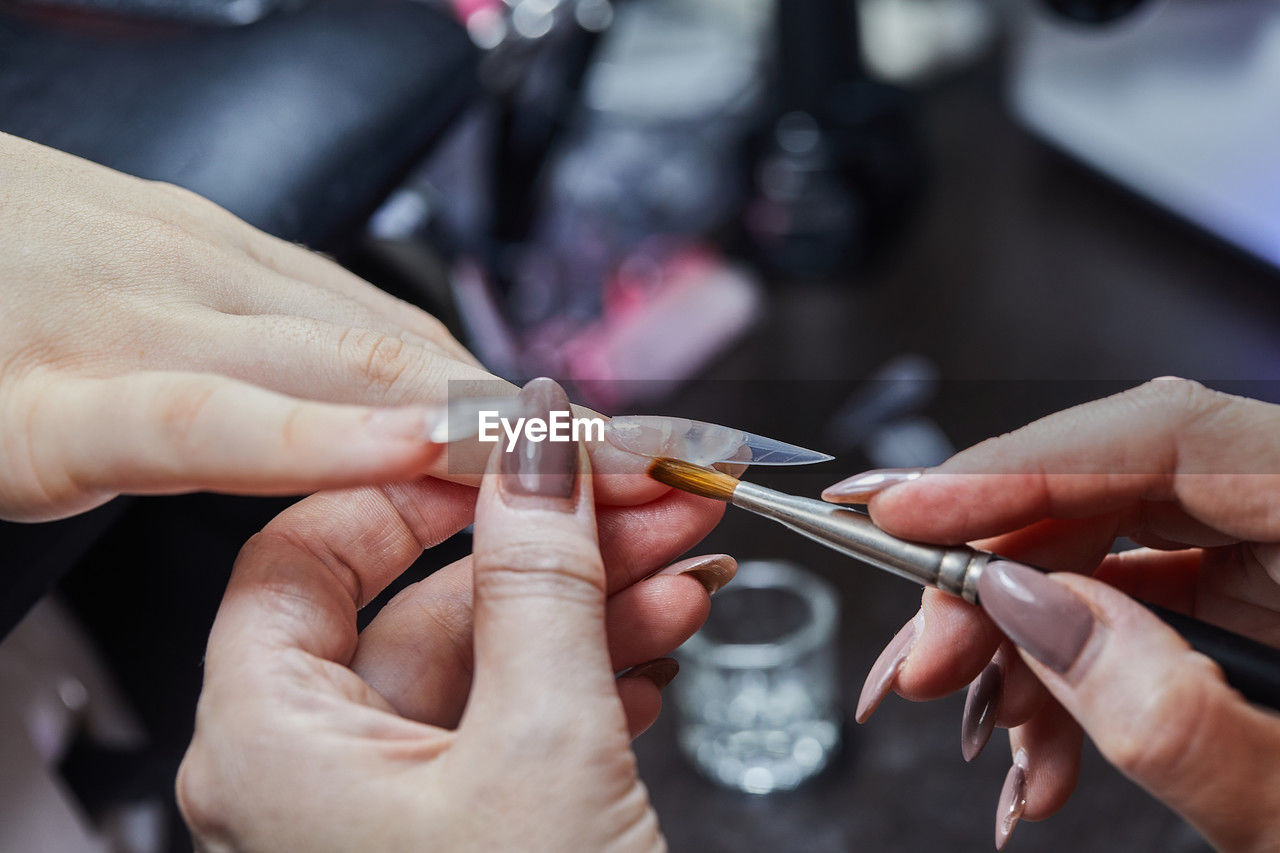 hand, adult, two people, women, finger, skill, occupation, nail, indoors, holding, craft, manicure, business finance and industry, working, expertise, close-up, female, business, men, focus on foreground, customer, small business