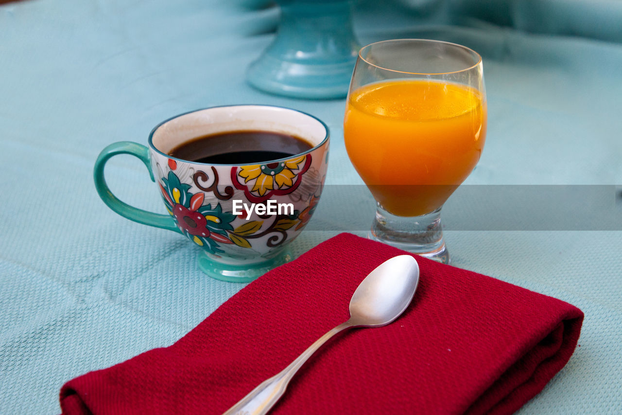 Black coffee in a colorful flower print cup with orange juice on a blue table cloth