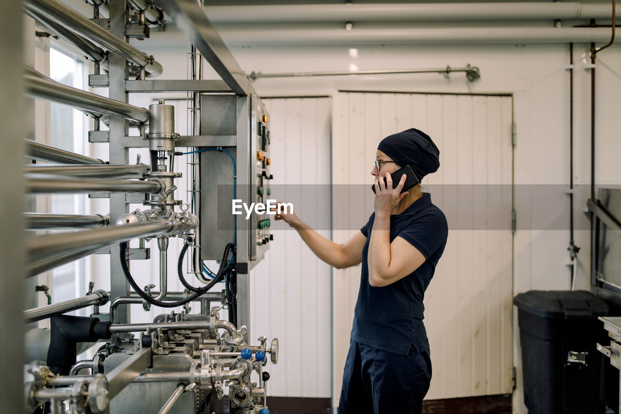 Farmer operating machine and talking on smart phone at dairy factory