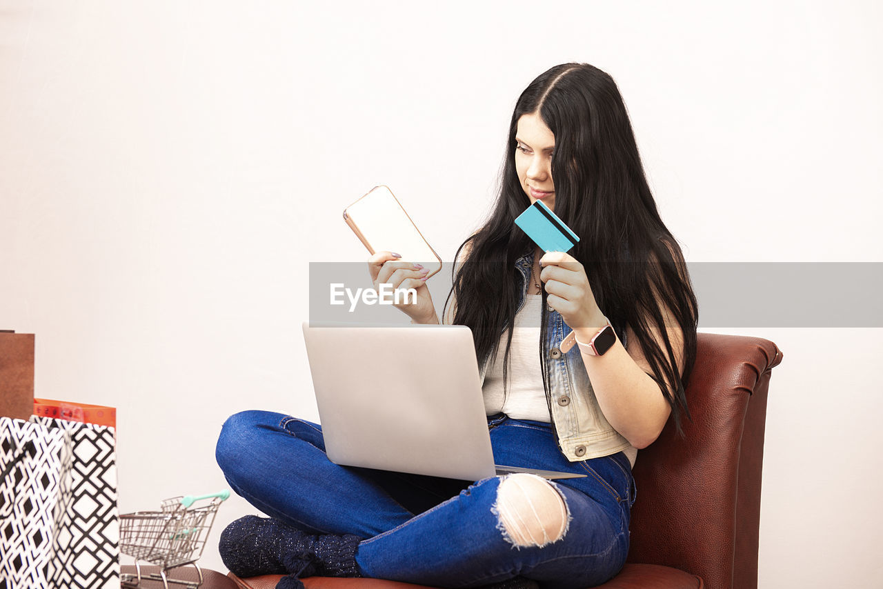 MIDSECTION OF WOMAN USING PHONE WHILE SITTING ON WALL