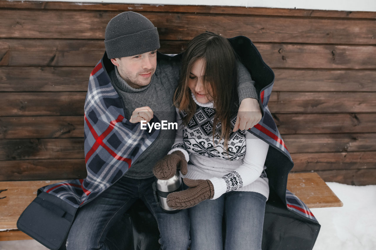Couple embracing while sitting on bench during winter