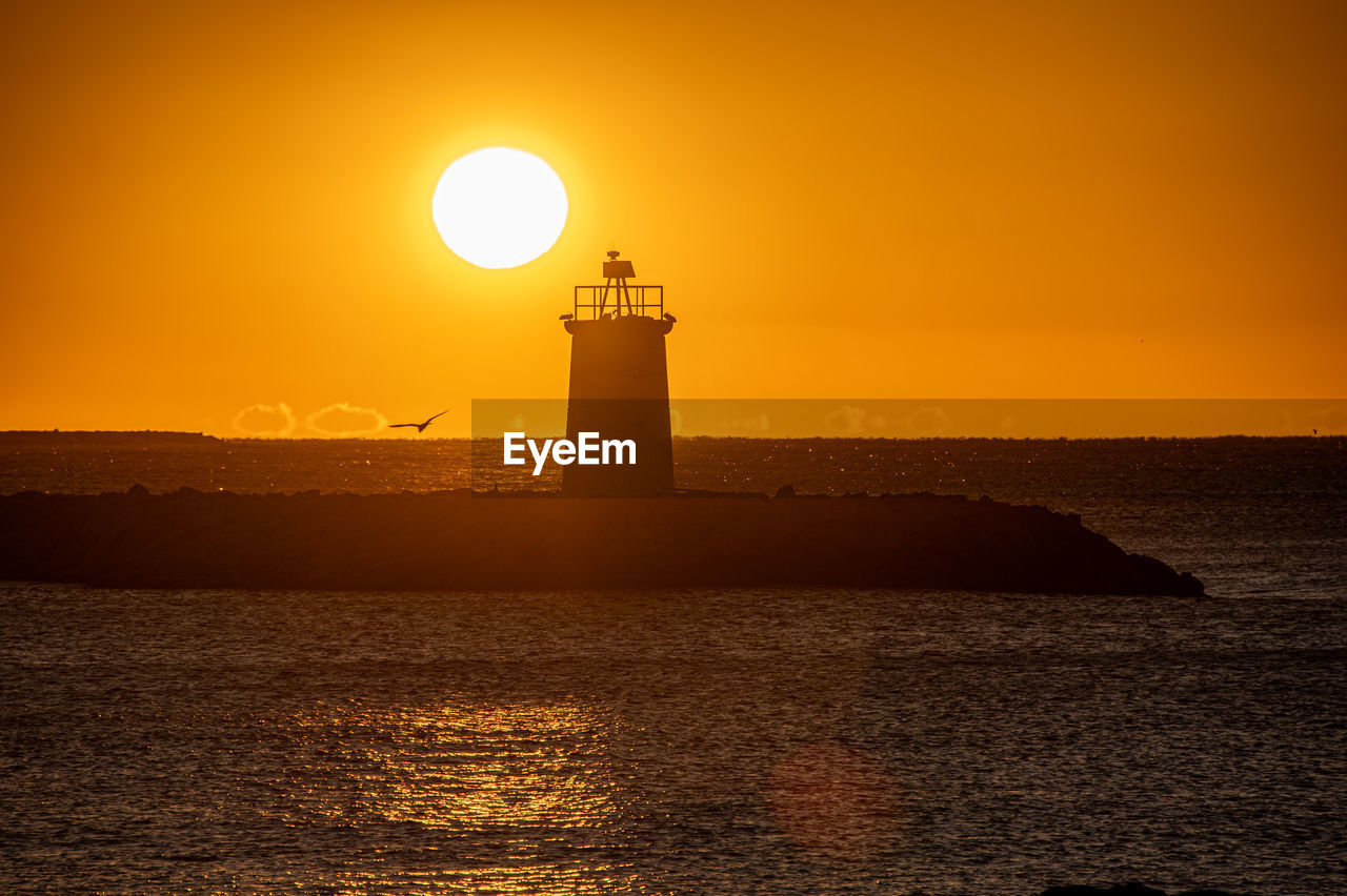 lighthouse by sea against clear sky during sunset