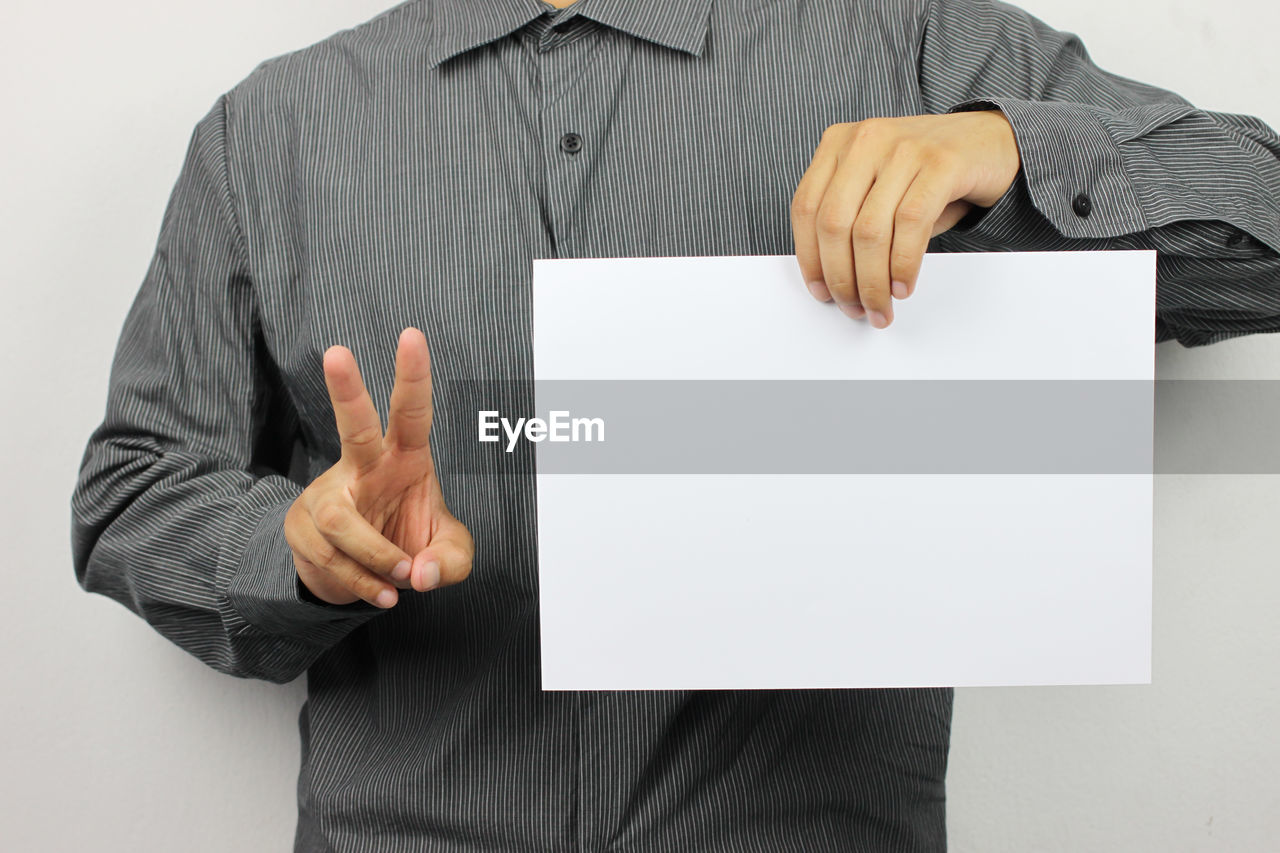 Midsection of businessman holding blank paper against white background