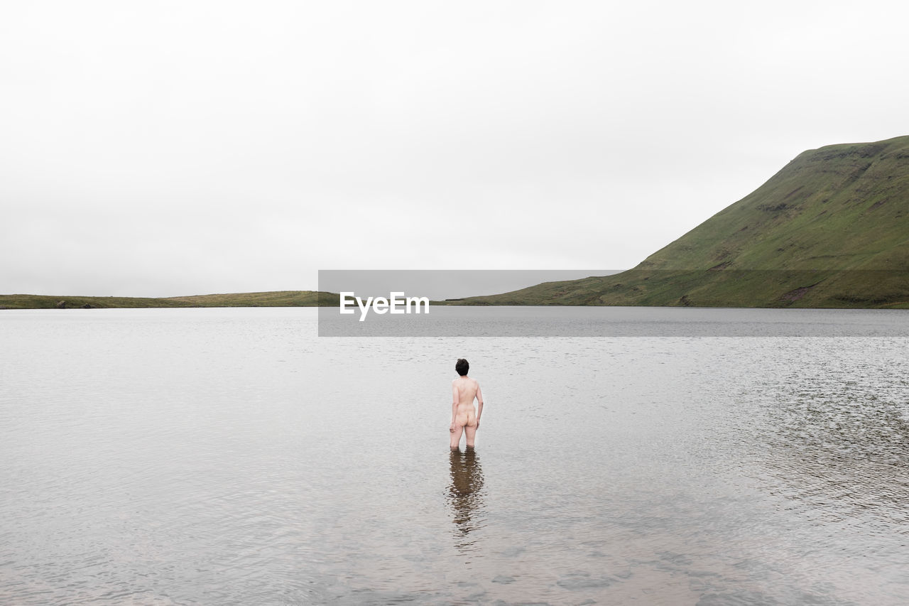 Naked man standing in lake against sky