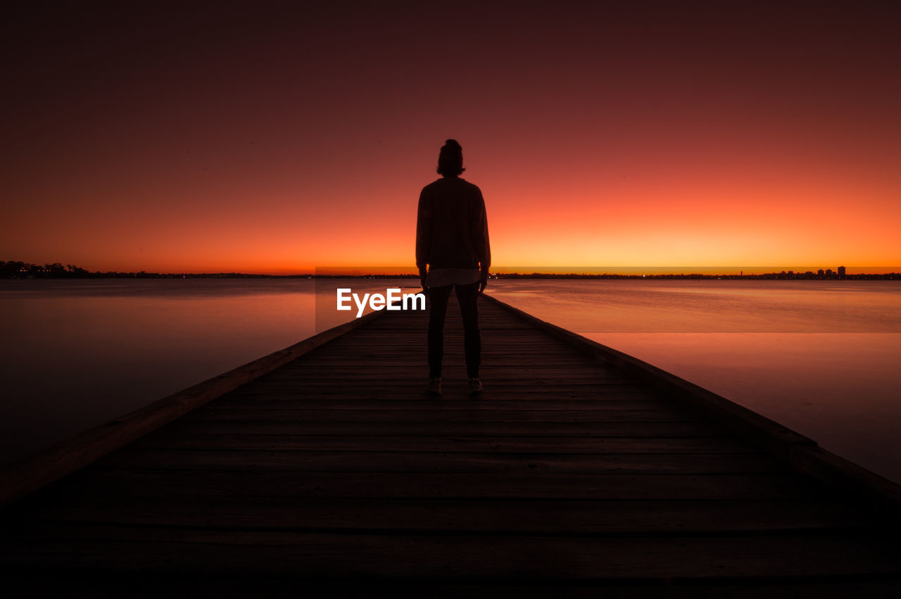 Silhouette man standing on pier over sea during sunset