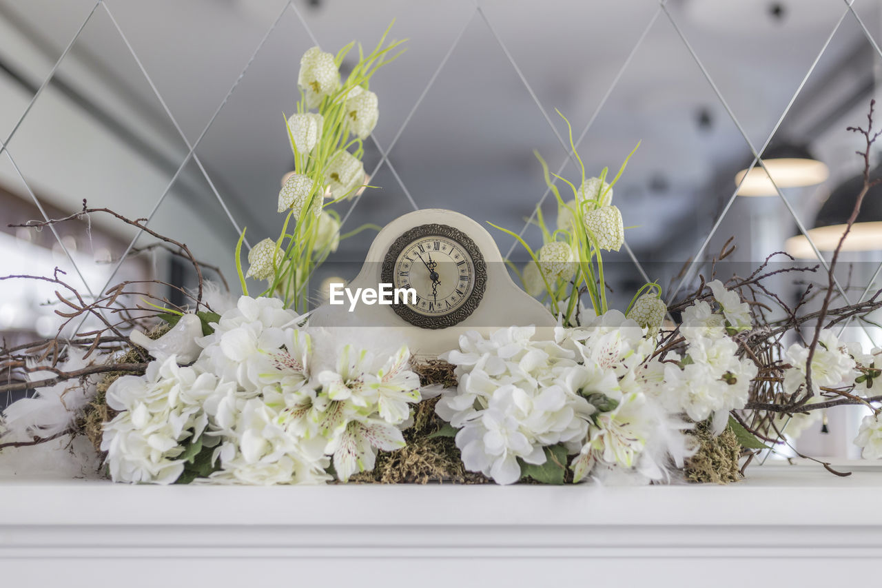 Clock with white flowers against patterned mirror
