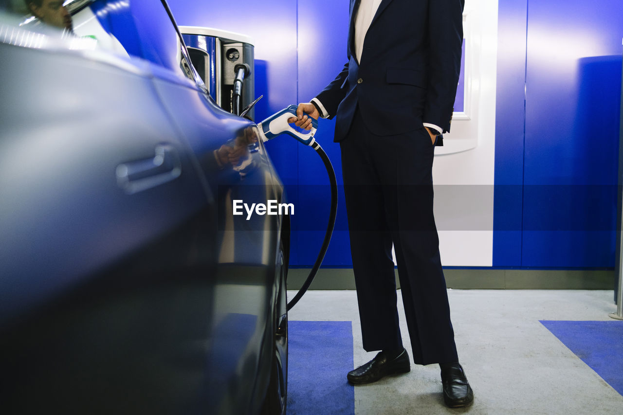 Businessman with hand in pocket charging electric car at station