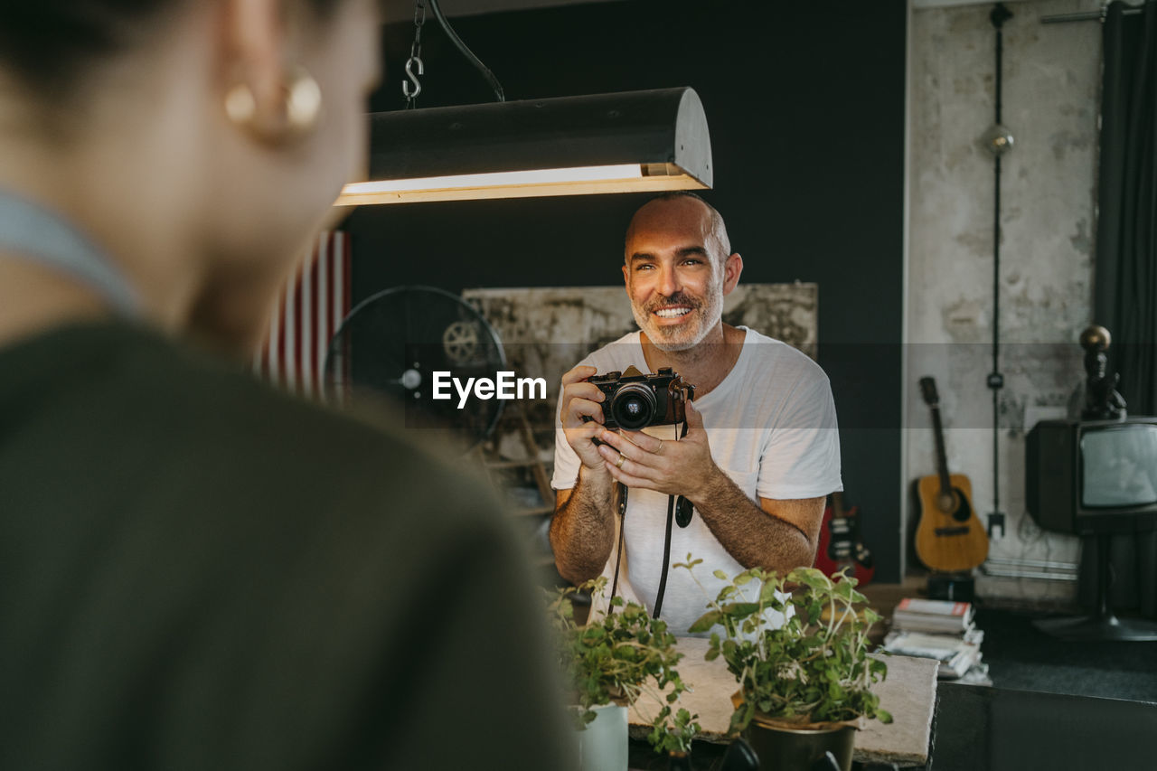 Happy male photographer holding digital camera while looking at colleague in studio