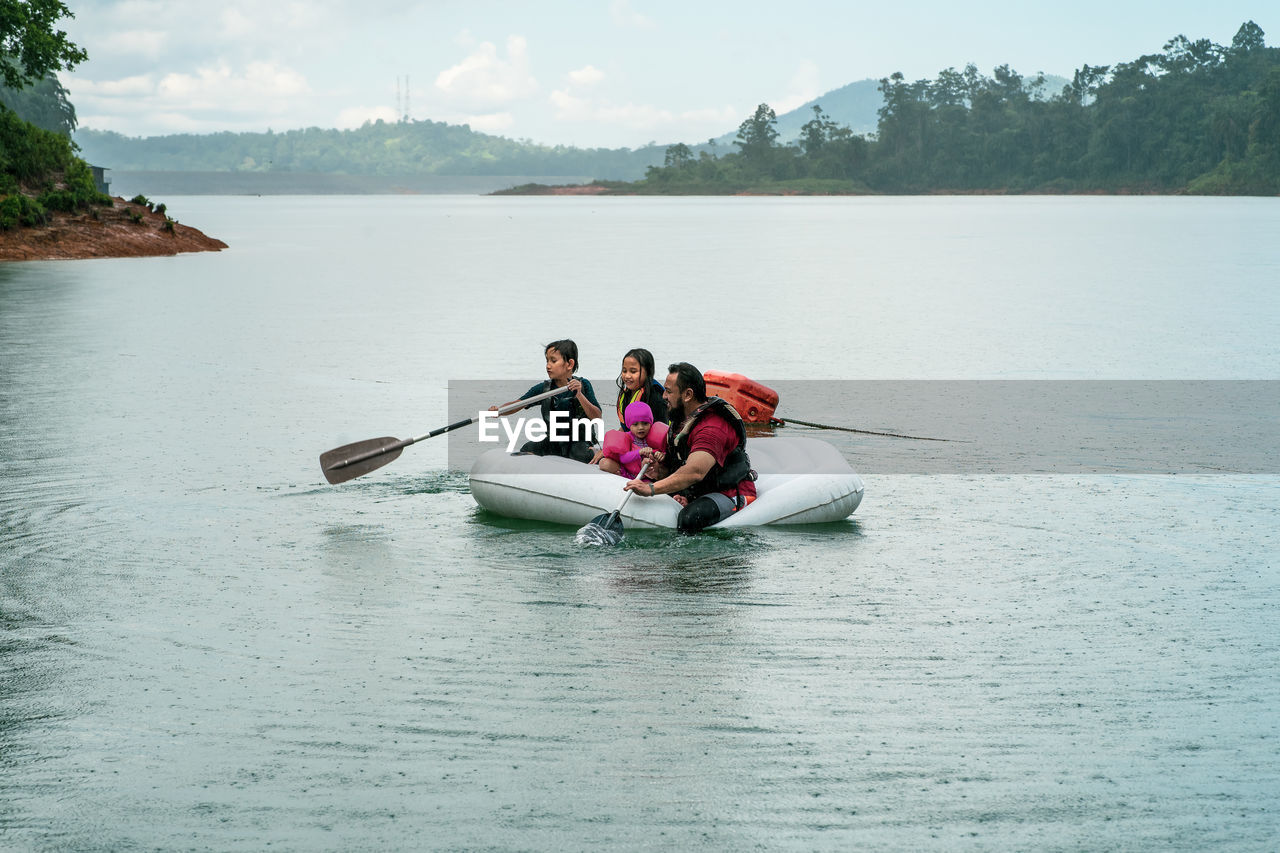 Family wearing life jackets paddling on an inflatable boat in kenyir lake, malaysia.