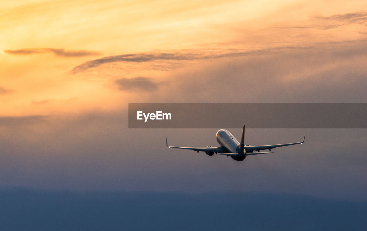 Low angle view of airplane flying against sky during sunset