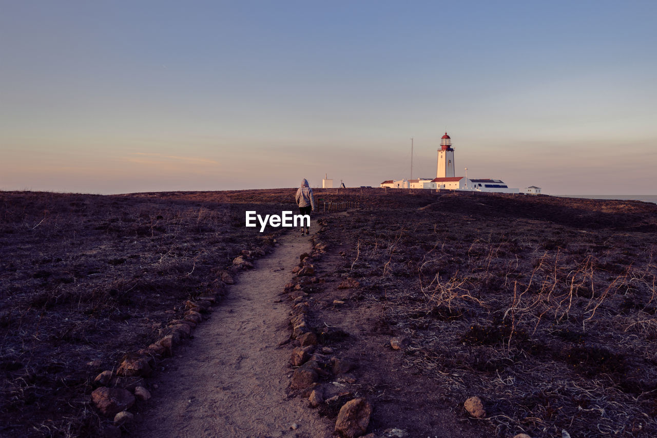 Scenic view of woman walking on landscape against sky during sunset