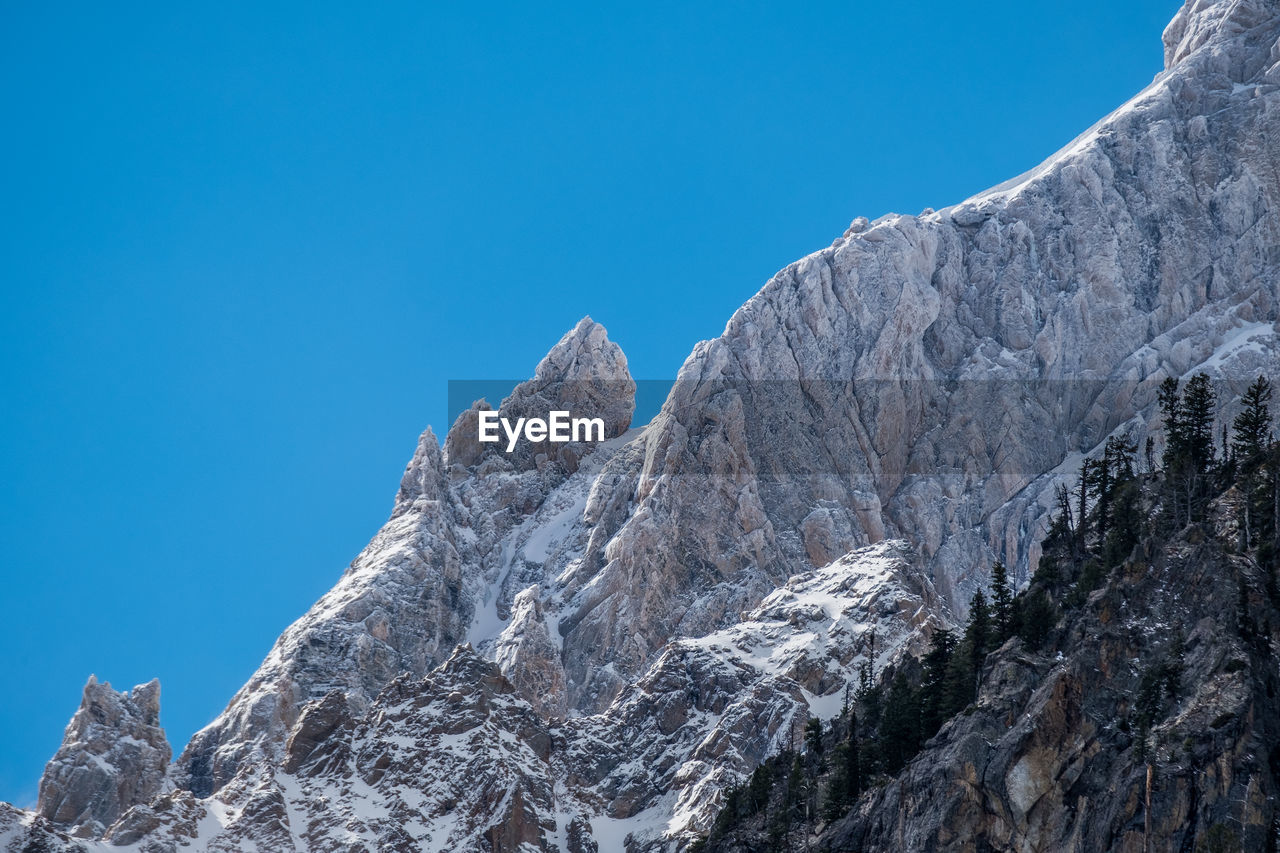 Low angle view of snowcapped mountains against clear blue sky