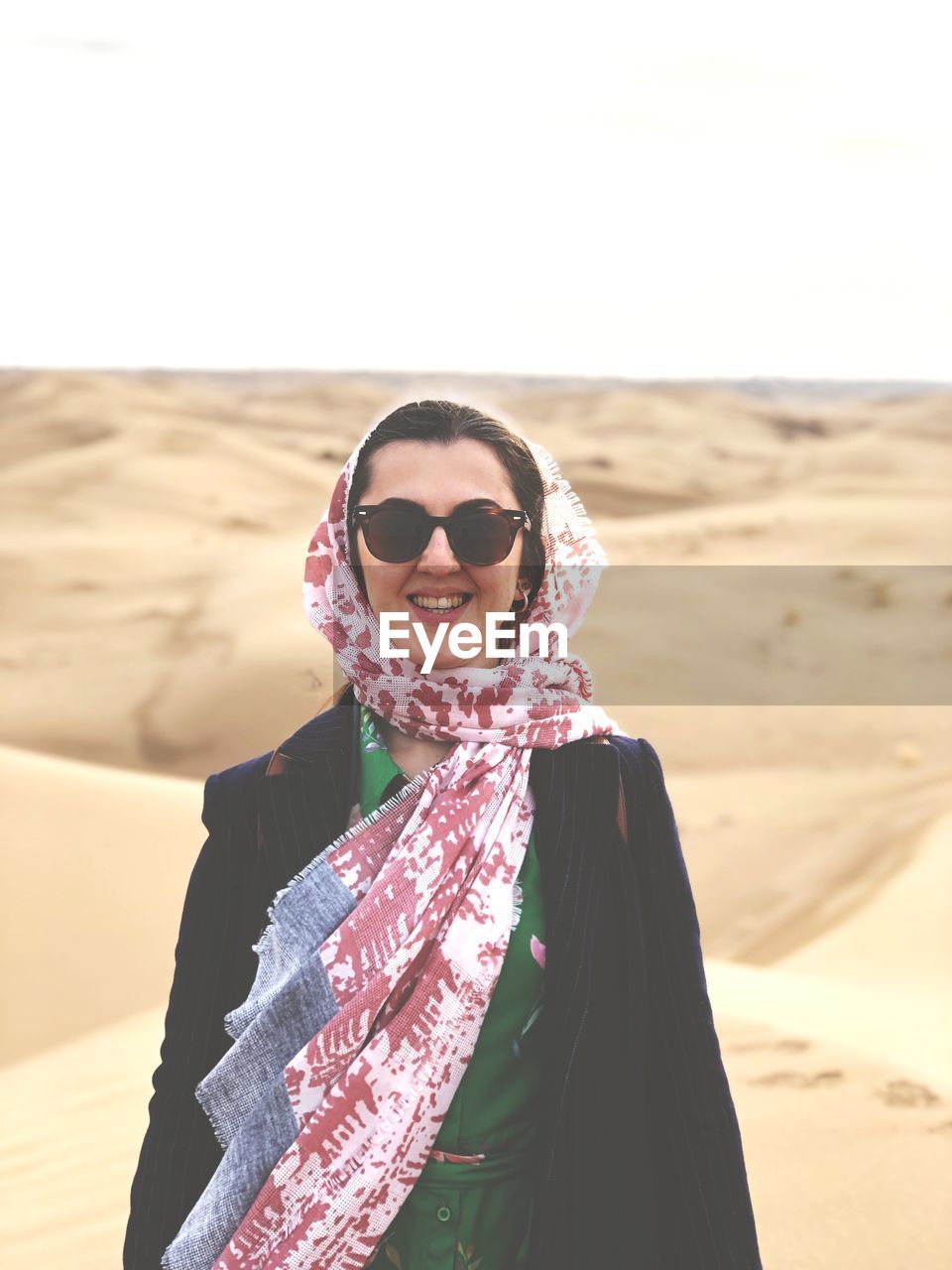 Portrait of smiling young woman in headscarf standing at desert