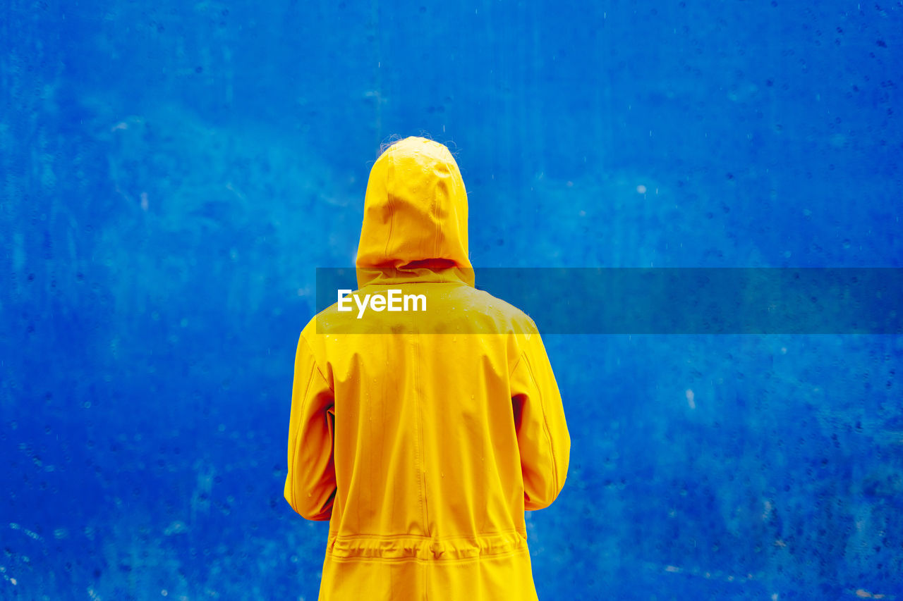 Rear view of person wearing raincoat against blue wall