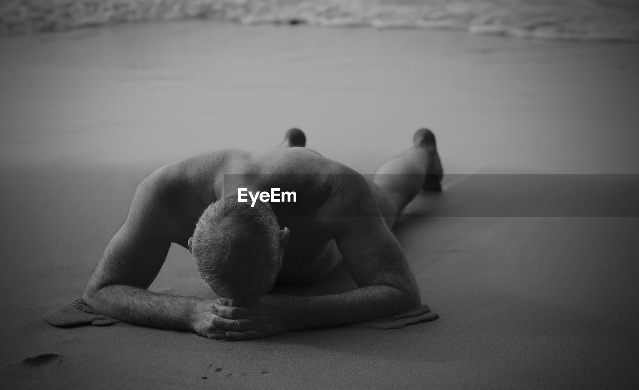 Rear view of shirtless man having sunbathing on beach