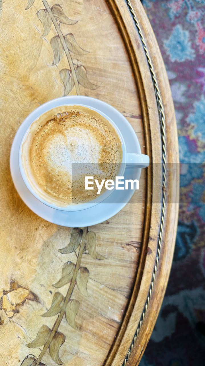 Top view of cup of cappuccino coffee with latte art on wooden table background.