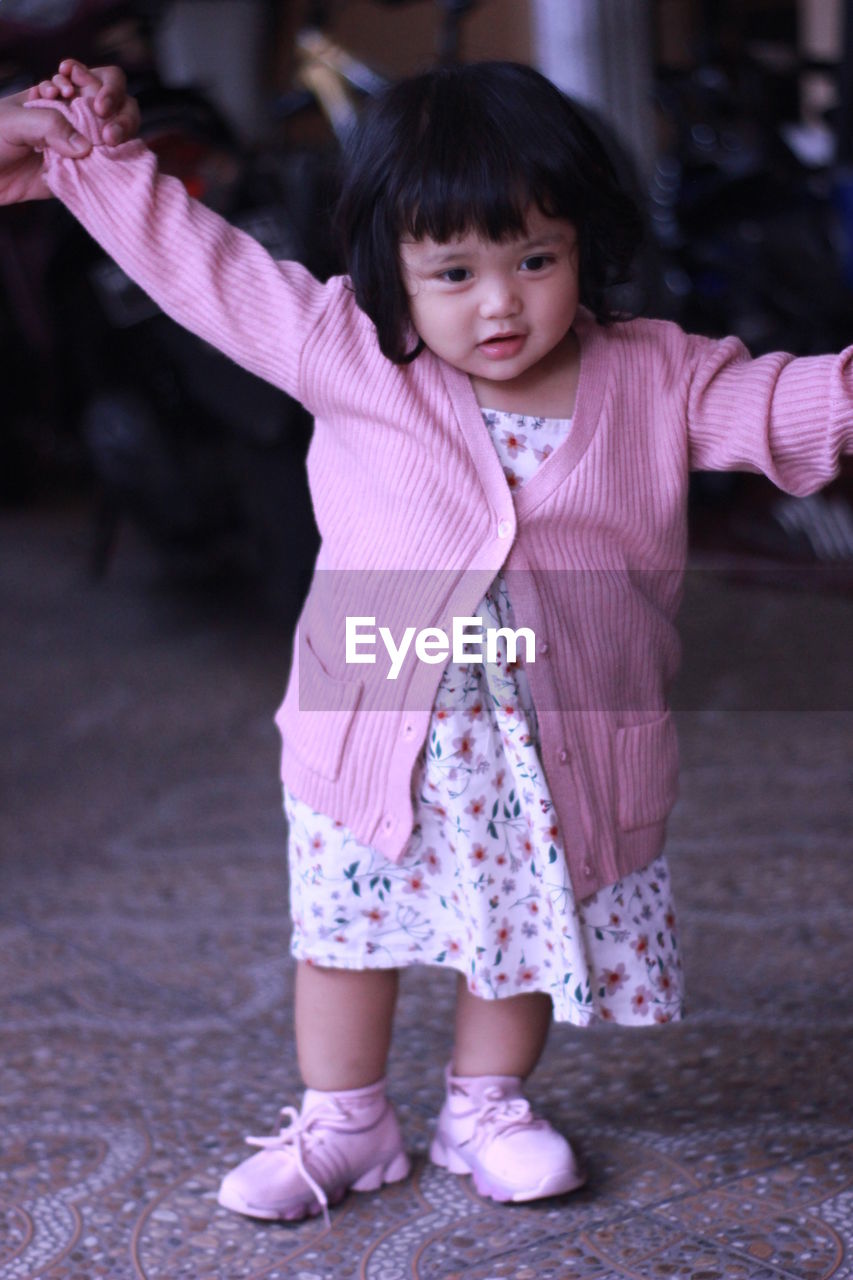 Full length of cute girl standing on pink umbrella