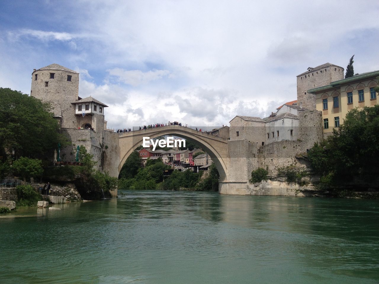 Arch bridge over river by buildings against sky